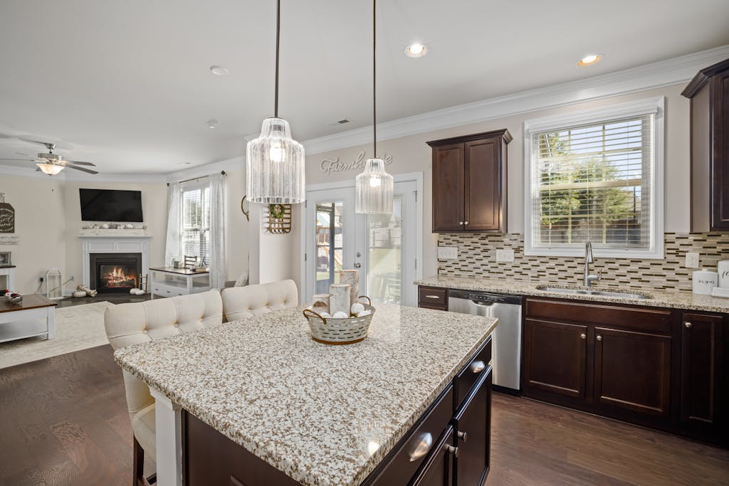 Bright kitchen featuring a granite island, dark wood cabinets, and ambient lighting.