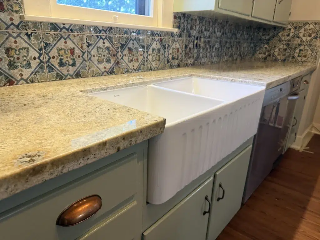 granite countertops with a farmhouse sink. with light green cabinets 