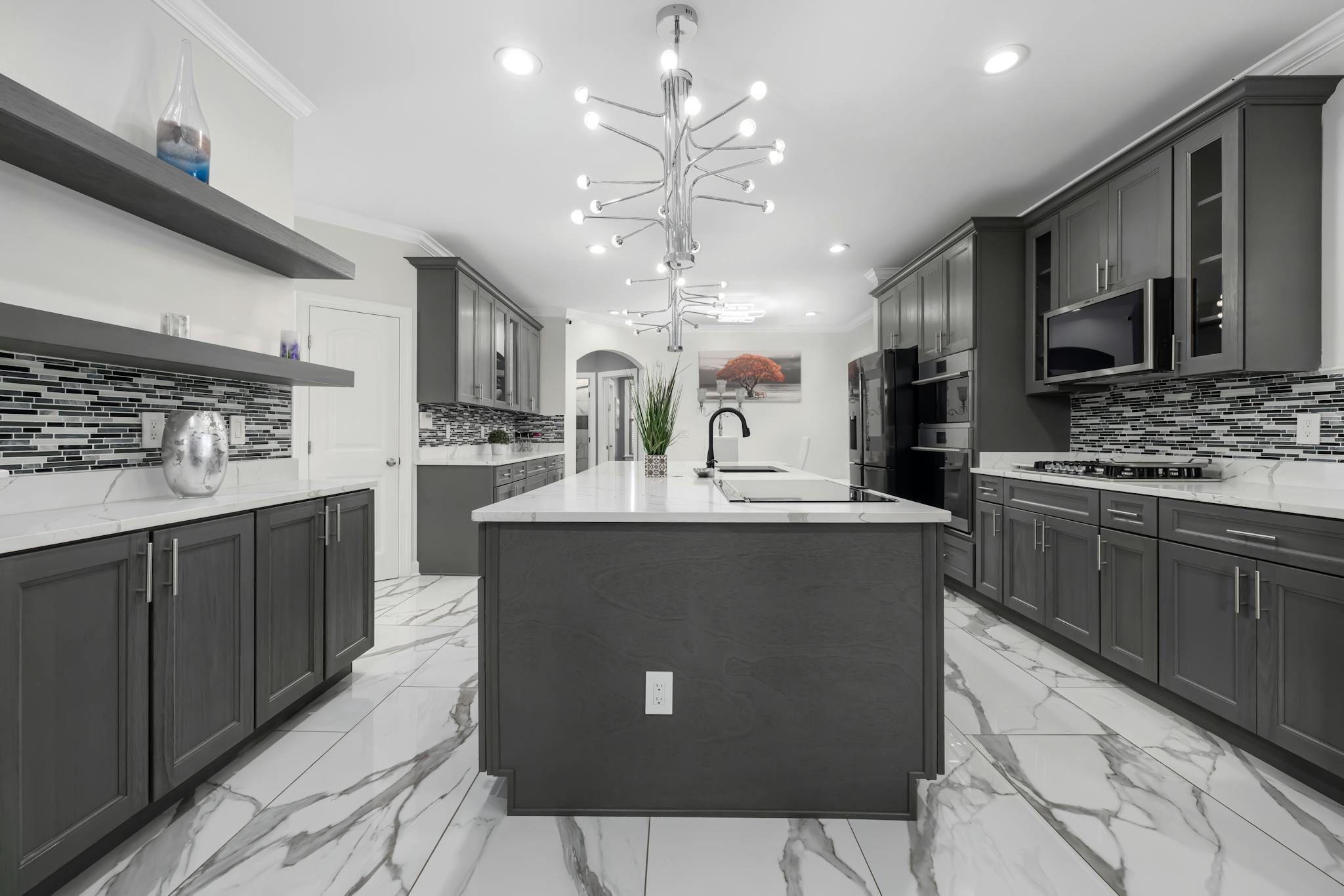 Spacious modern kitchen with grey cabinets and marble floors, featuring contemporary lighting.